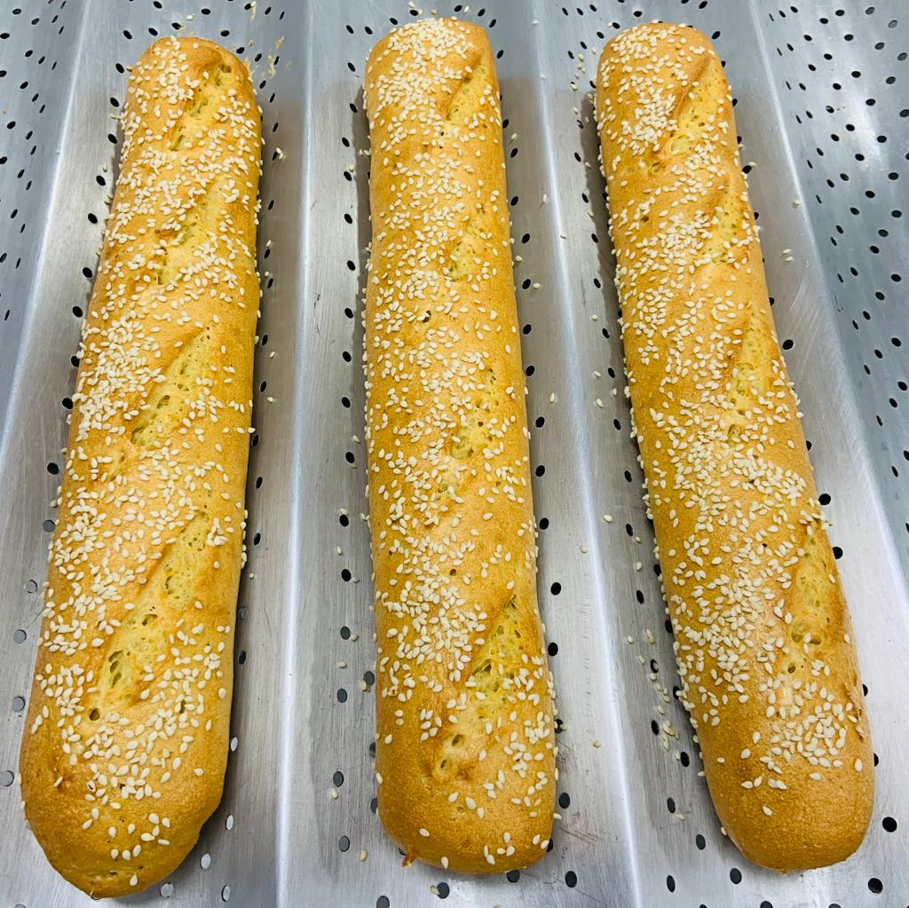 Sobre una bandeja perforada, tres panes tipos baguette sin gluten, decorado con semillas de ajonjolí.