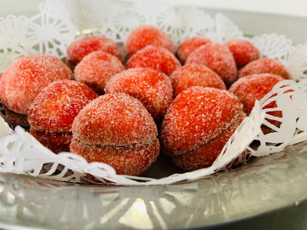 Dos galletas con harinas alternativas, rellenas con mermelada o dulce de leche, decorado con colorante rojo y azúcar.