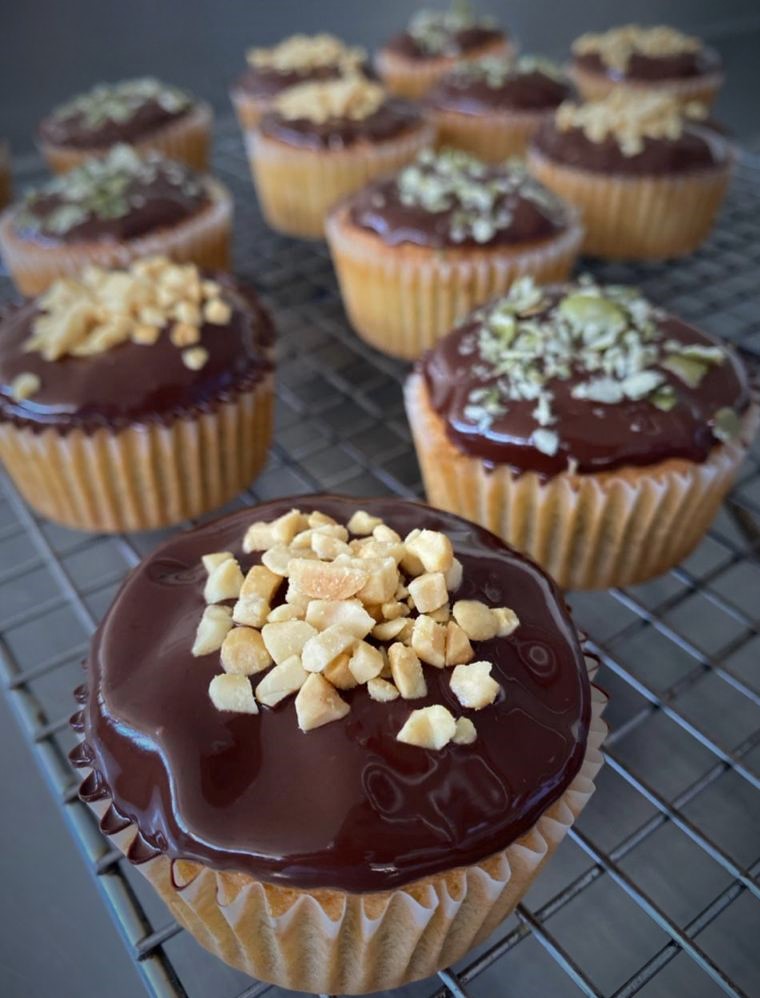 Se observan varios cup cake decorados con cobertura de chocolate, sobre esta cubierta maní y pistachos.